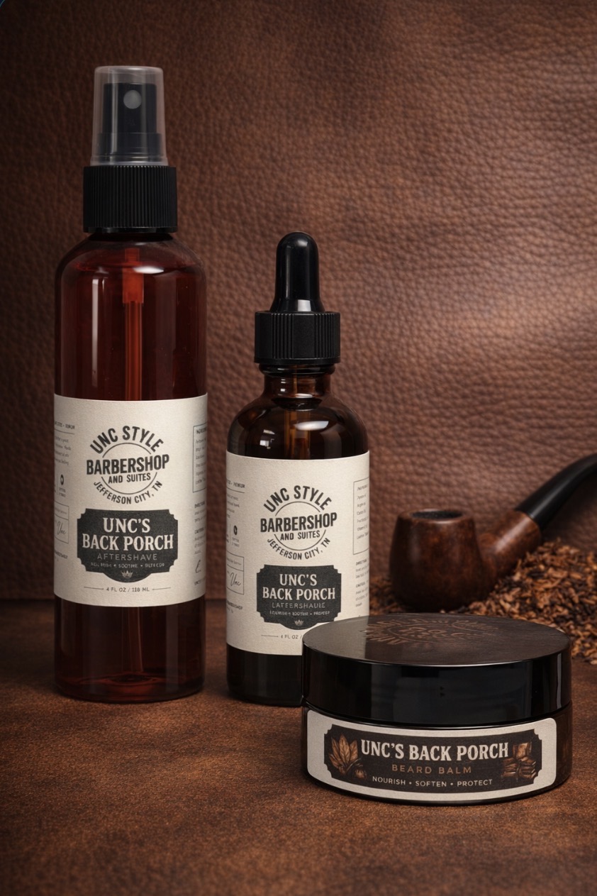 Unc's Back Porch aftershave spray, beard oil dropper bottle, and beard balm jar on a leather backdrop with a tobacco pipe